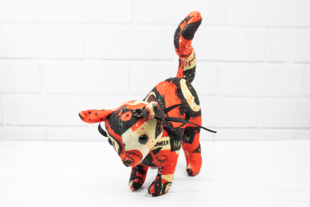 Plush toy cat with Halloween-themed pattern on a white background