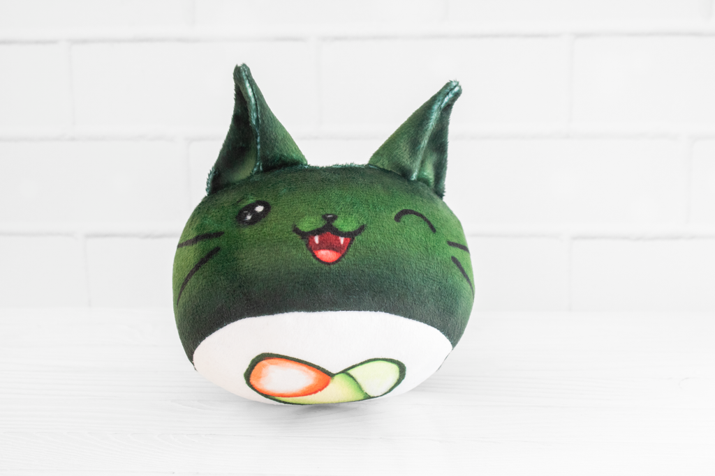 A handmade green plushie cat in the shape of a sushi roll with green ears and a white tail sticking out. It has a kawaii face with one eye winking and an open pink mouth that shows cat fangs. The top and the bottom have a white base and an image of a california roll's fillings in the shape of a heart. 